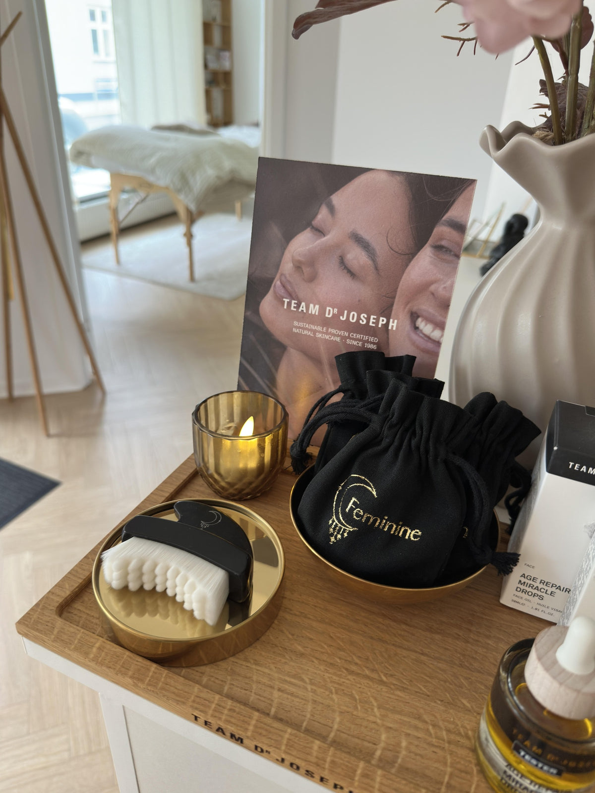 Feminine lymfebørste og gua sha på guldfad i butikken med klinikken i baggrunden
